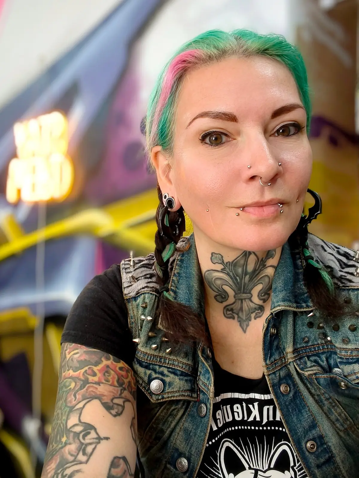 Mandy von Riot Candy mit grün-pinken Haaren, Piercings und Nieten-Jeansweste