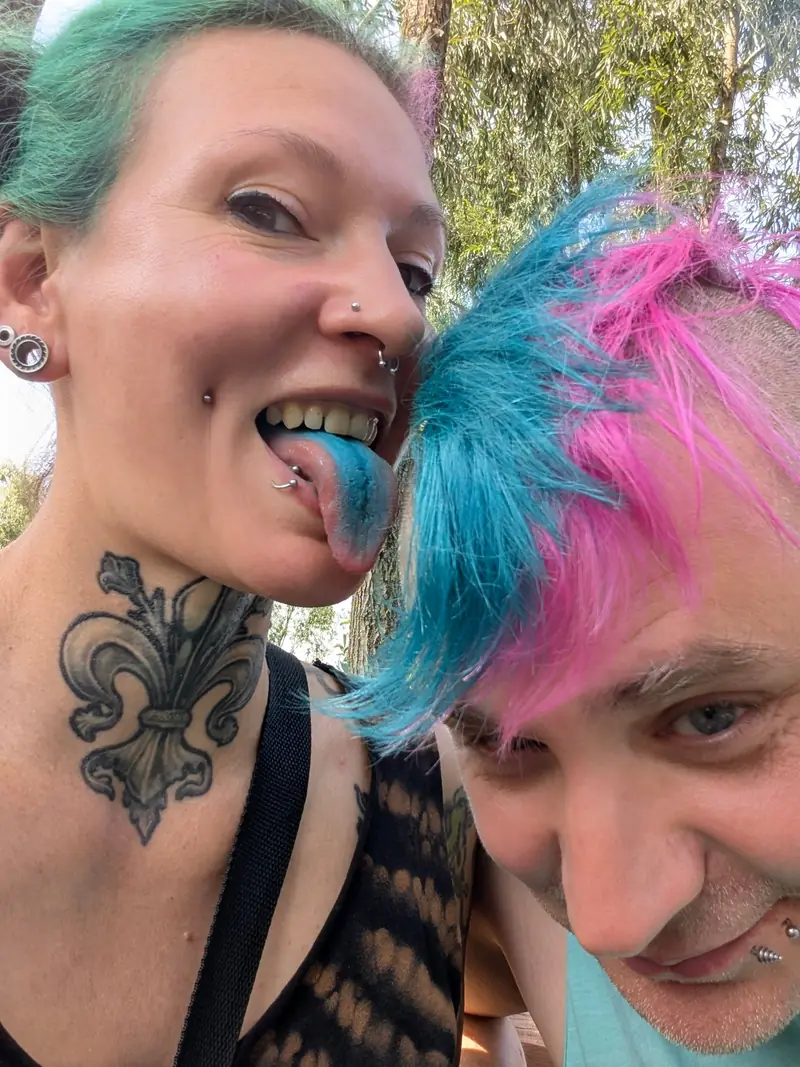 Selfie: Frau mit tätowiertem Hals und Mann mit pink-blauem Iro