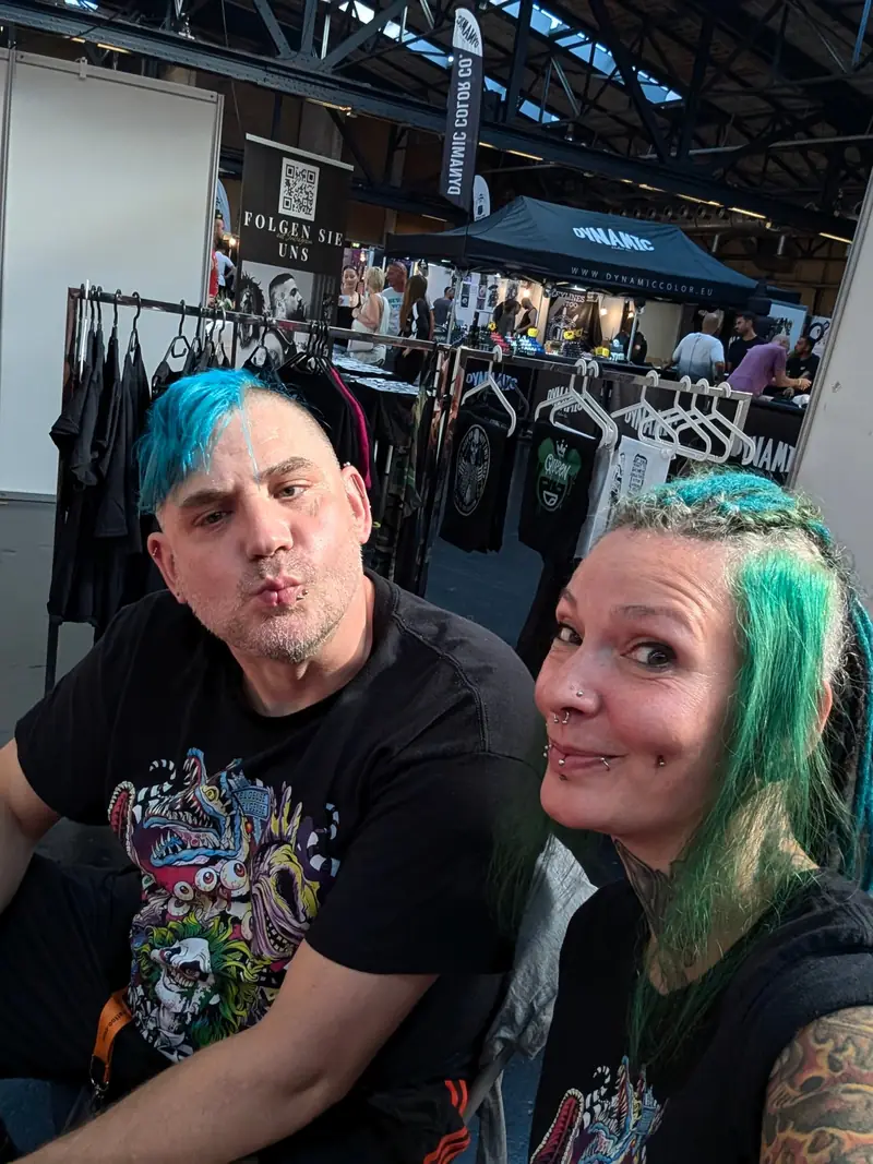 Zwei Leute mit bunten Haaren vor einem Stand voller Shirts