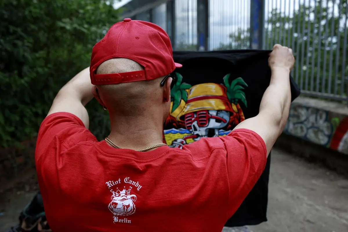 Mann im roten Riot Candy Berlin Shirt hält ein frisch bedrucktes Shirt hoch